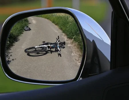 Bike lying on a road viewed through a car's side mirror, depicting a car and bike accident scene.